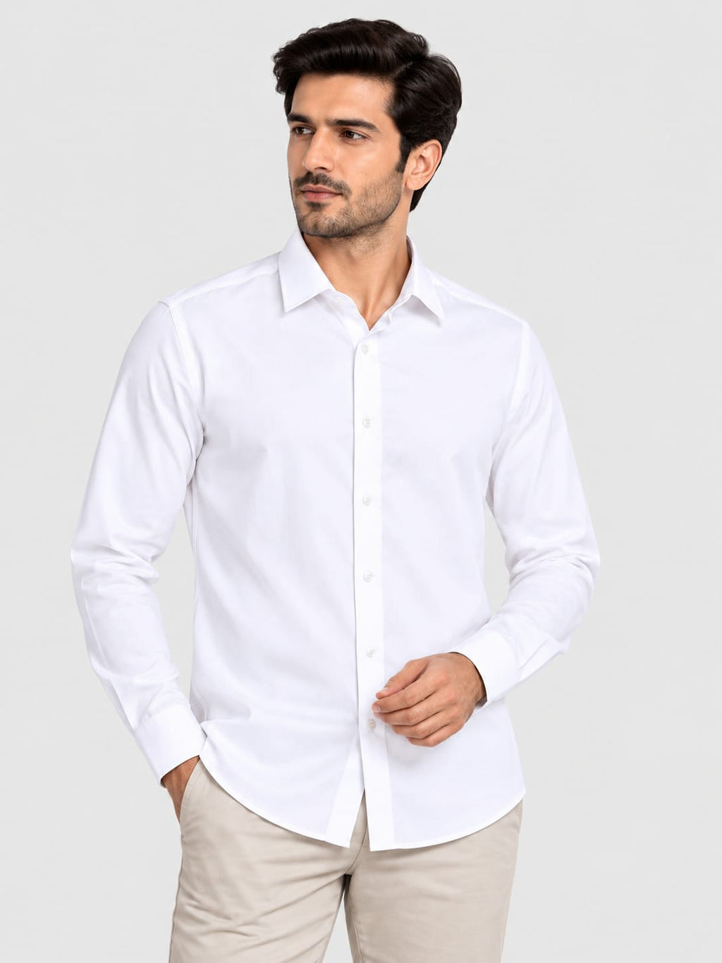 A man wearing a white long-sleeve button-down dress shirt and beige trousers, standing against a light gray studio background.