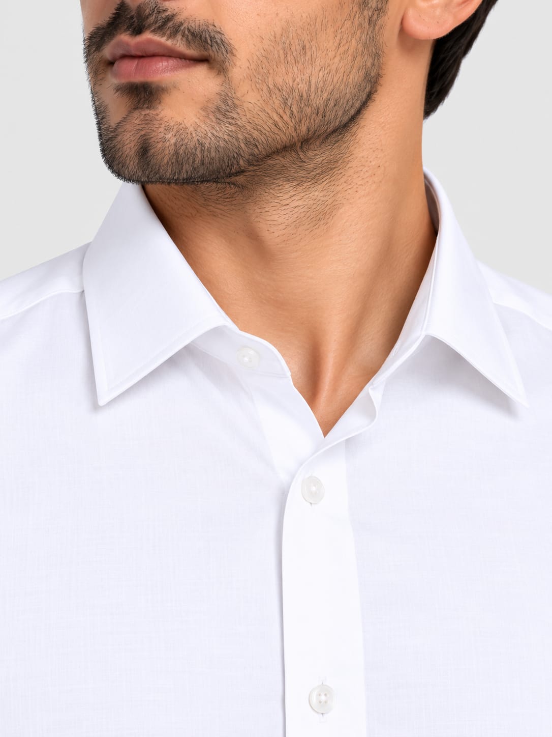 Close-up of a man wearing a white long-sleeve button-down dress shirt, showing the collar, chest area, and part of his lower face against a light gray background.