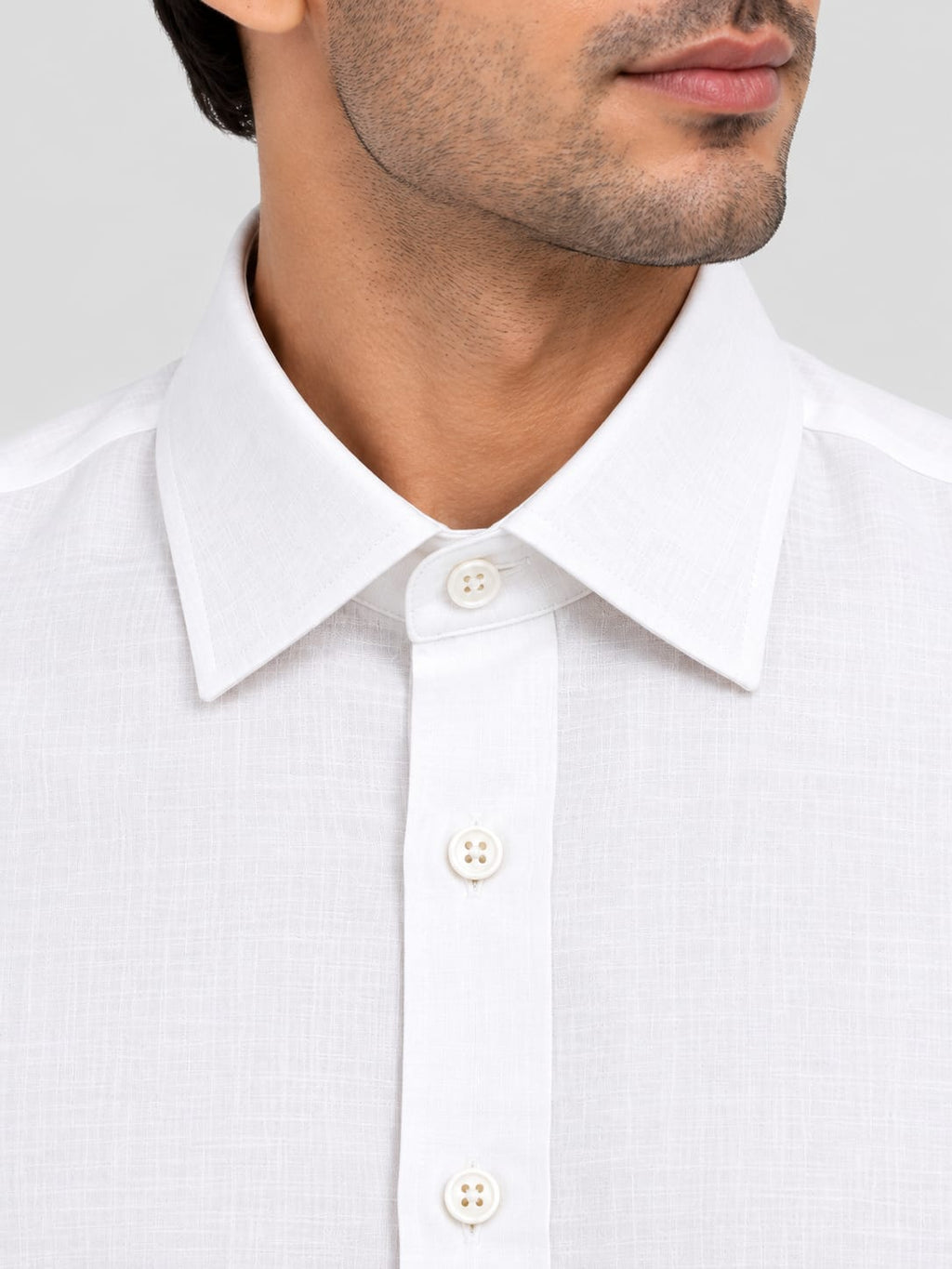 Close-up of a man wearing a white long-sleeve button-down shirt with a classic pointed collar and white buttons, set against a light gray background.