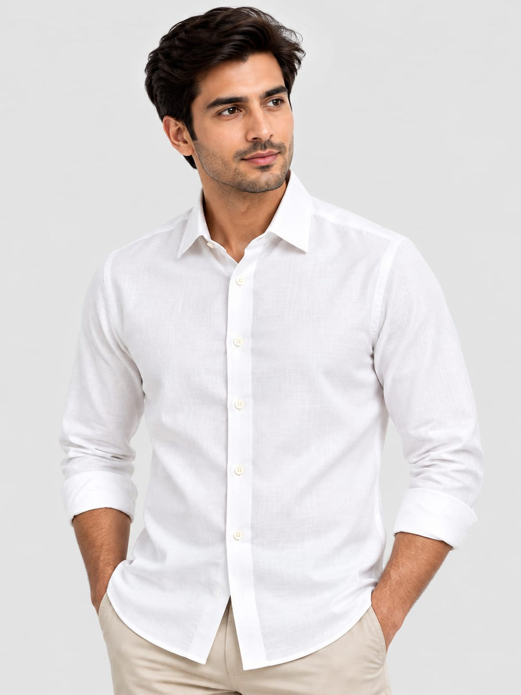 A man wearing a white long-sleeve linen button-down shirt with beige trousers, standing against a light gray studio background.
