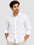 A man wearing a white long-sleeve linen button-down shirt with beige trousers, standing against a light gray studio background.