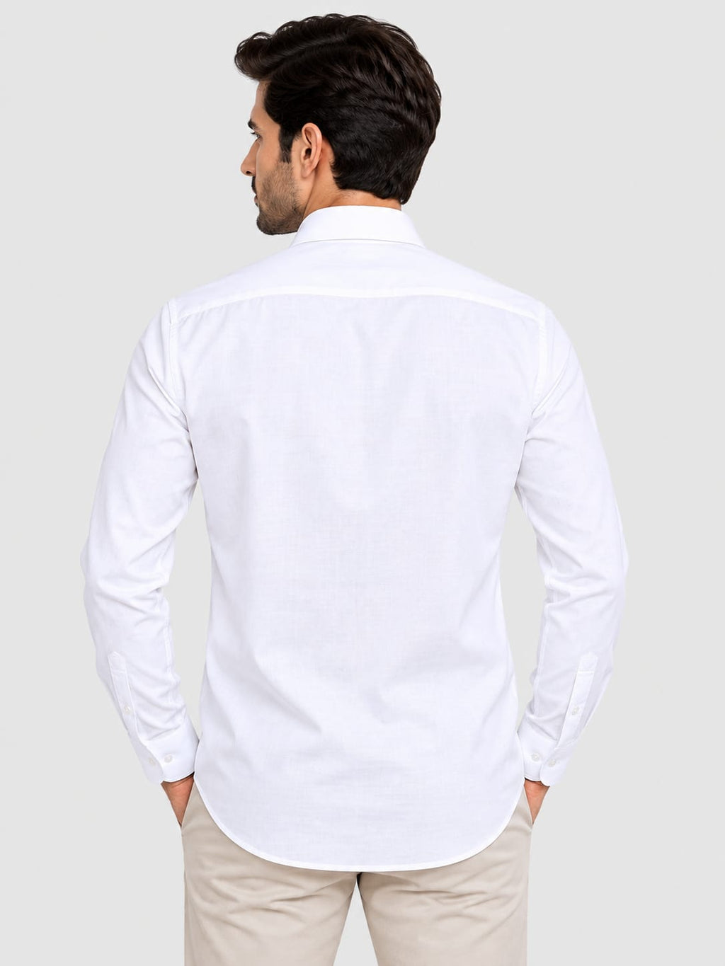 A man viewed from the back wearing a white long-sleeve button-down shirt and beige trousers, set against a solid light gray background.