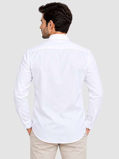 A man viewed from the back wearing a white long-sleeve button-down shirt and beige trousers, set against a solid light gray background.